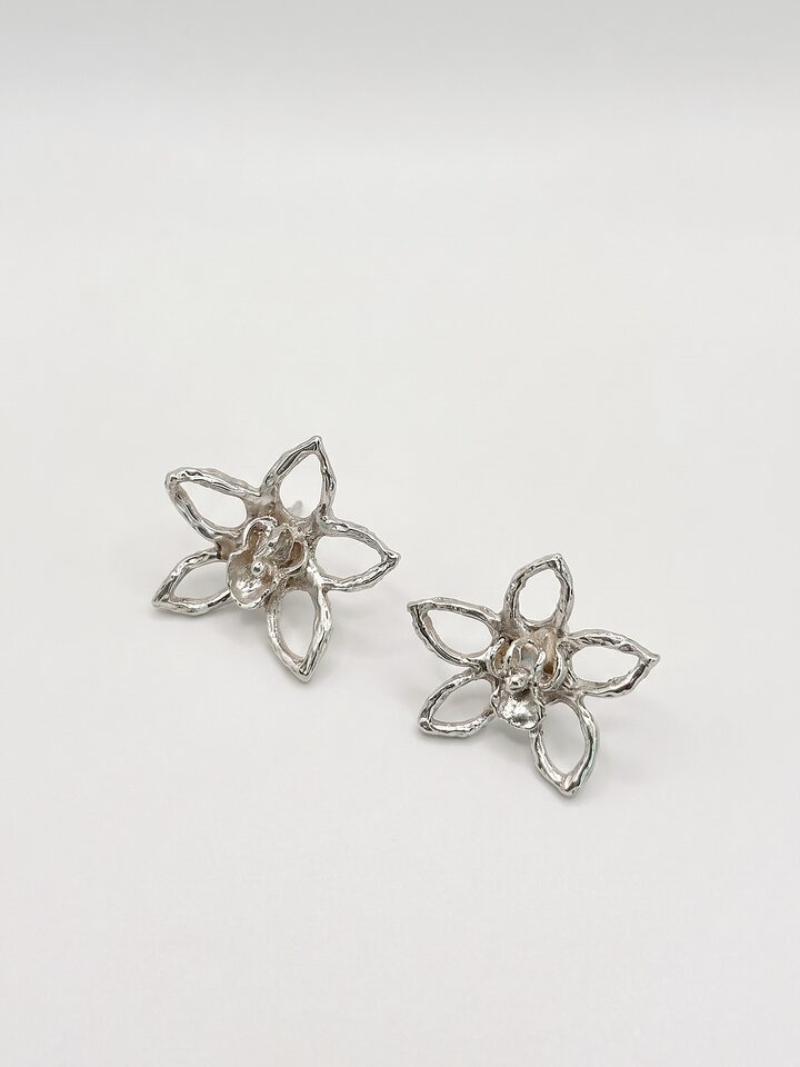 Pair of large silver open five-petal flower stud earrings with small textured blossoms at their centres, on a white background.