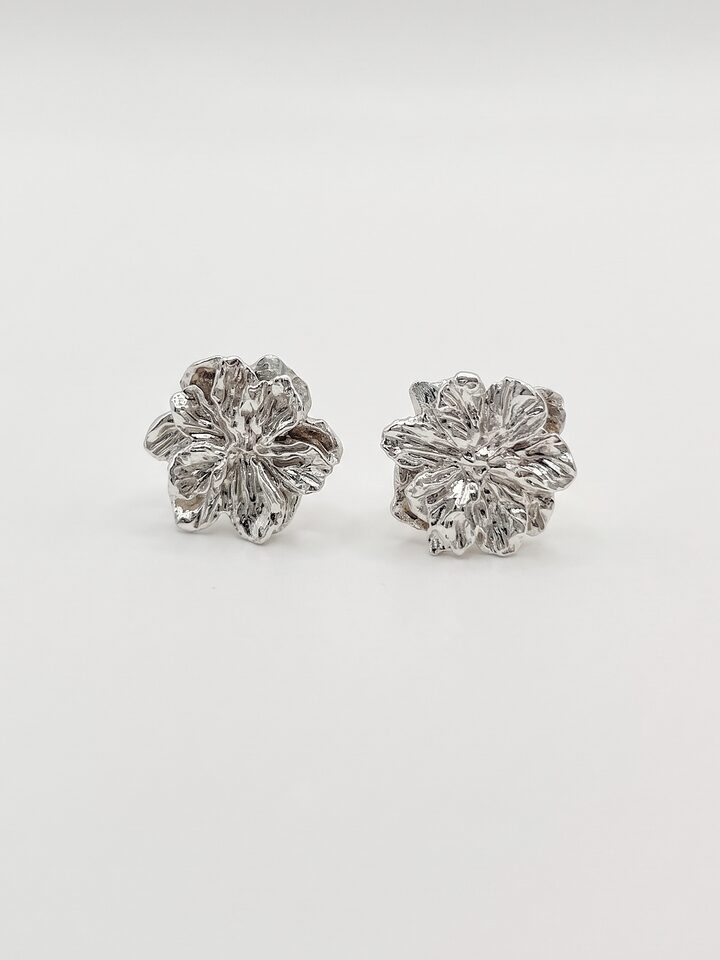 Pair of textured silver flower stud earrings with layered, veined petals, on a white background.