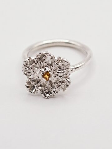 Silver flower ring with textured ruffled petals and a small yellow sapphire at the centre, on a round silver band, on white.