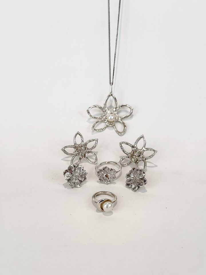 Silver flower jewelry on white: open flower pendant with a pearl, two pairs of flower earrings, a flower ring with a yellow sapphire and a pearl ring.