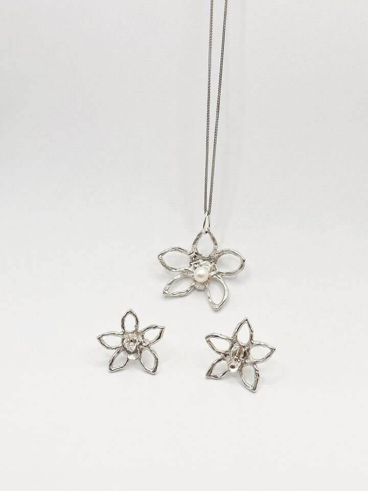 Silver open five-petal flower pendant with a white pearl on a fine chain, with two matching open flower stud earrings, on white.