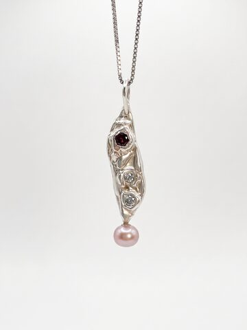 Long textured silver pendant with a small red stone and two small diamonds above a pink pearl drop, on a silver box chain, on white.