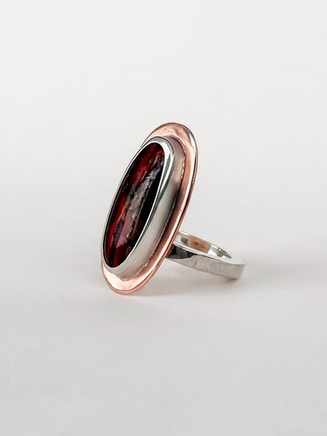 Silver ring with a large oval deep red stone in a copper frame, on a white background.