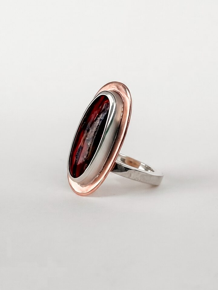 Silver ring with a large oval deep red stone in a copper frame, on a white background.