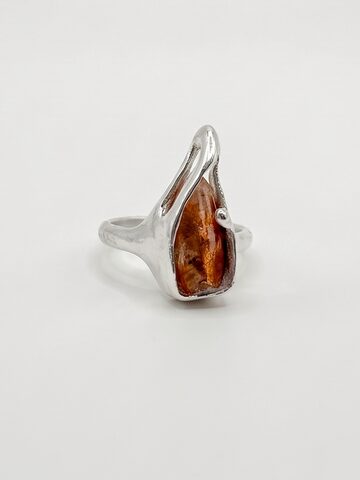 Silver ring with a raw orange sunstone held by organic silver prongs, on a white background.