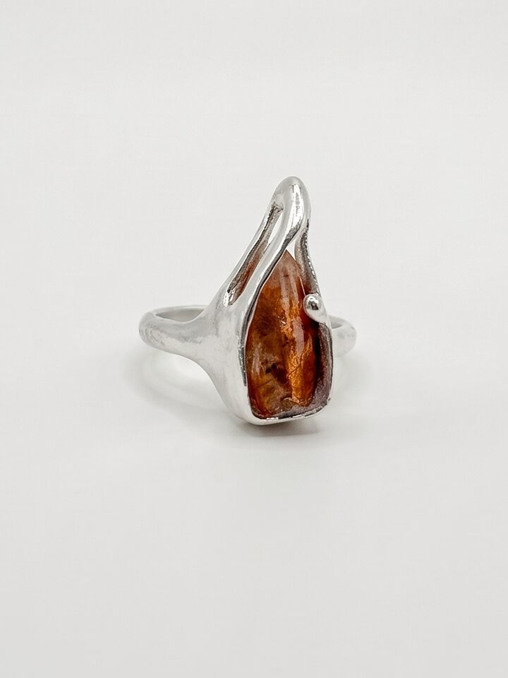 Silver ring with a raw orange sunstone held by organic silver prongs, on a white background.