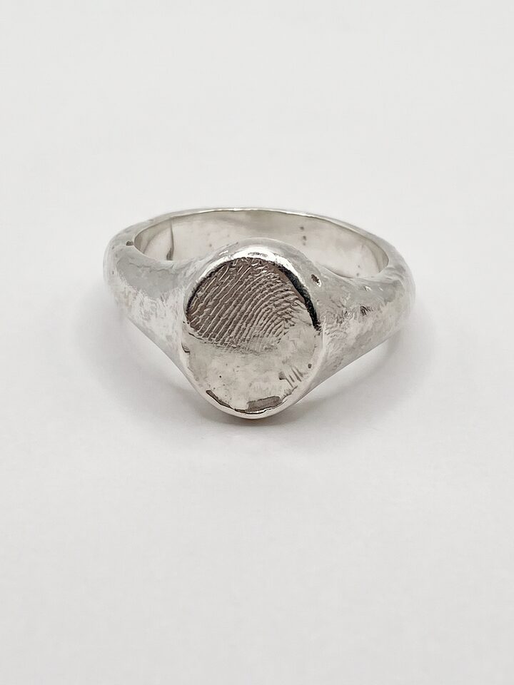 Chunky organic silver signet ring with a fingerprint impression on its oval face, on a white background.