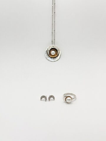 Silver disc pendant with a white pearl on a golden brass inner disc, crescent moon stud earrings and a silver pearl ring, on white.